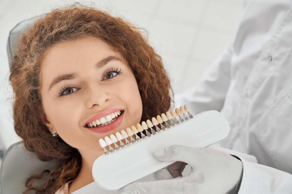 Paciente sorridente na Paridaens Odontologia em Perdizes comparando a cor branca de suas lentes de contato dental com uma escala de tons.