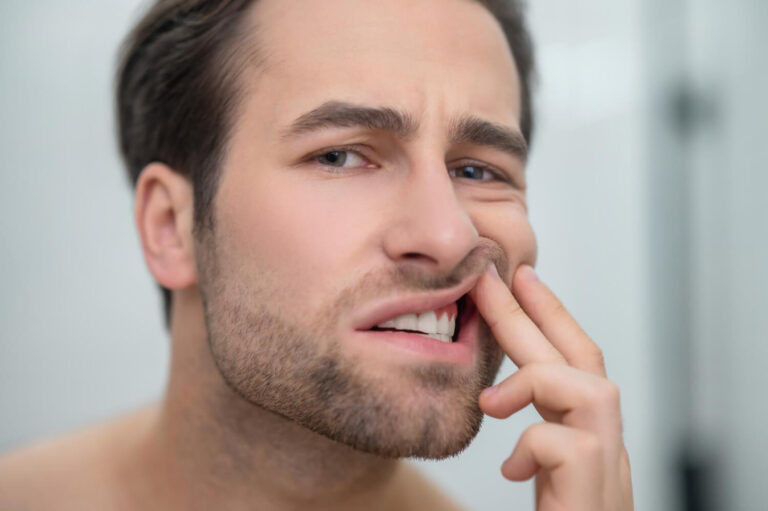 Homem com expressão de dor afasta o lábio mostrando a gengiva na Clínica Paridaens Odontologia em Sumaré, onde previne gengivite.