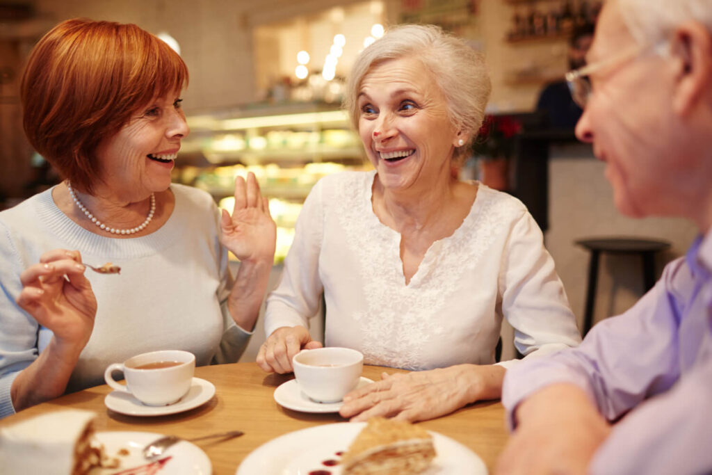Três idosos sorrindo enquanto comem sobremesa em uma cafeteria, celebrando a mastigação confortável com prótese protocolo em Sumaré.