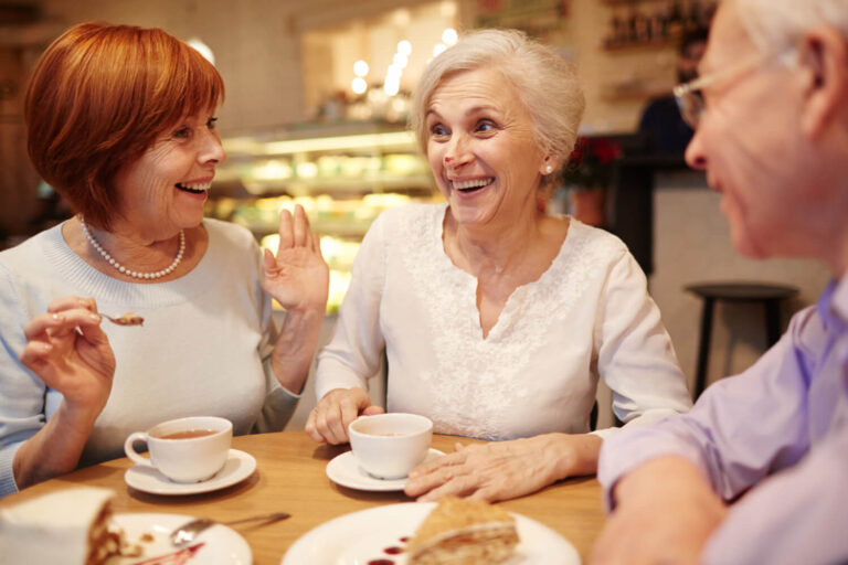 Três idosos sorrindo enquanto comem sobremesa em uma cafeteria, celebrando a mastigação confortável com prótese protocolo em Sumaré.